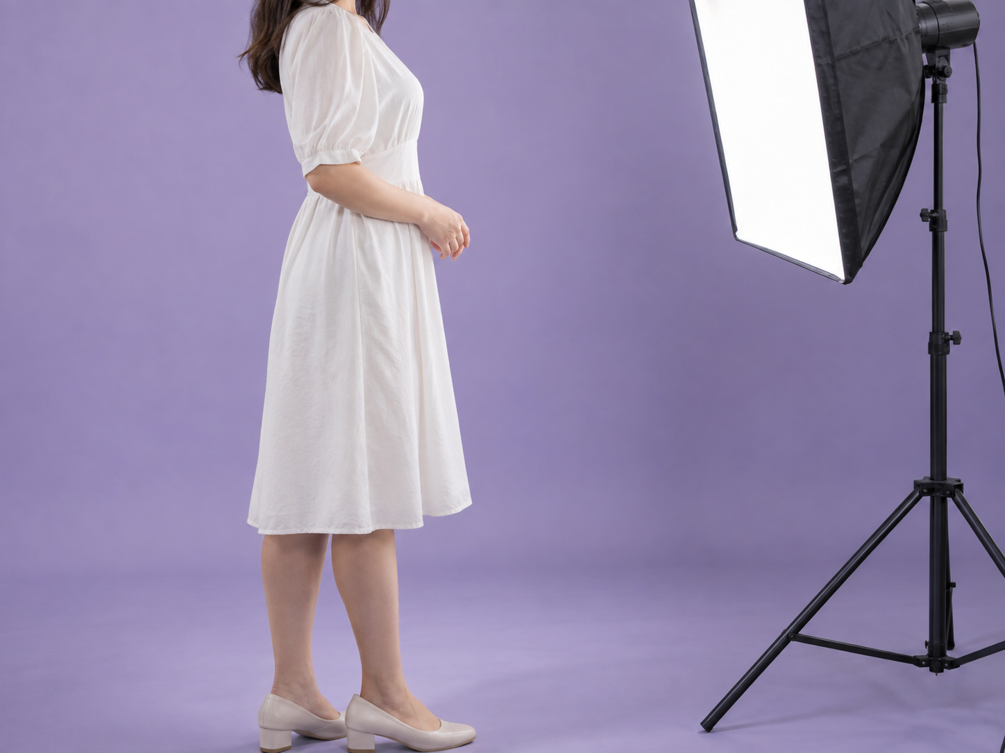 Adult woman in a white dress standing beside a studio light with her face outside the frame